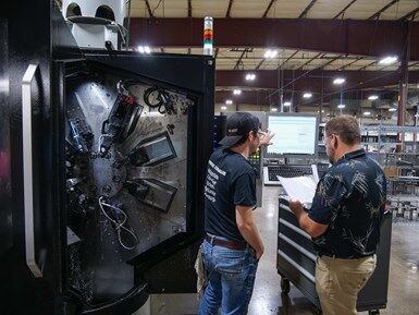 Two Mitotec employees work at a multi-spindle machine with the work envelope exposed