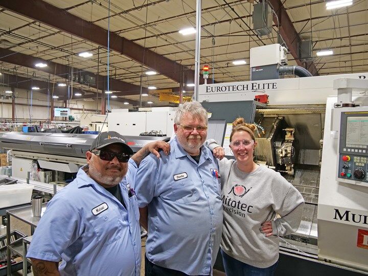 Three Mitotec employees pose smiling in front of a Eurotech lathe